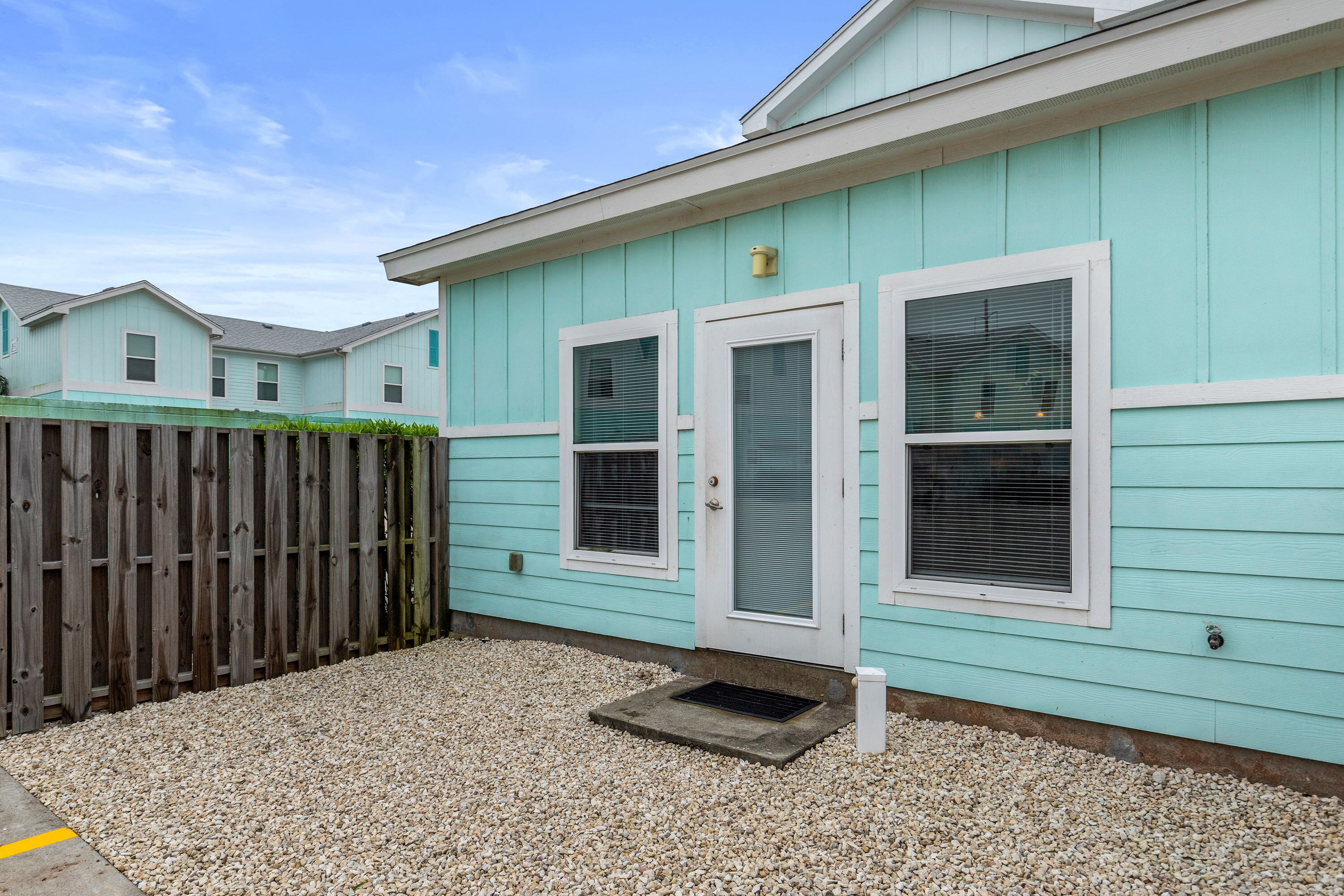 A row of light blue houses with white trim, wooden fences, and gravel ground.