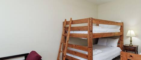 Une pièce propre et bien éclairée, avec un lit superposé, un lit simple, un banc en bois et une œuvre d’art représentant un hippocampe accrochée au mur.