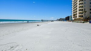 A beach with a pier extending into the ocean, a few people walking, and a tall building with balconies on the right. - Seasider 302 - Two-bedroom, Two & 1/2 Bath Oceanfront Condo (Garden City Beach)