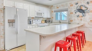A kitchen with white cabinets, a refrigerator, a microwave, a stove, and a sink. There are red stools at the counter.