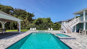 A rectangular swimming pool with a tiled deck, surrounded by lounge chairs and a covered seating area.