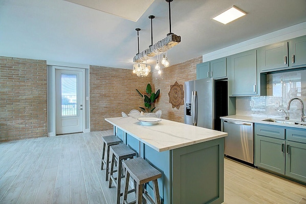 A modern kitchen with a central island, bar stools, a refrigerator, and a sink.