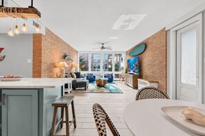 A modern kitchen with a dining area, a ceiling fan, and a large window.
