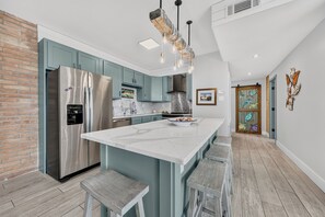A modern kitchen with a central island, stainless steel appliances, and a rustic brick wall.