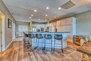 A spacious kitchen with a central island, bar stools, and a dining area with a table. - T's Treasure's - Eight-bedroom, eight-bath oceanfront duplex w/ pool (Surfside Beach)