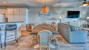 A modern kitchen with white cabinets, a wooden dining table surrounded by wicker chairs, and a grey sofa. - T's Treasure's - Eight-bedroom, eight-bath oceanfront duplex w/ pool (Surfside Beach)