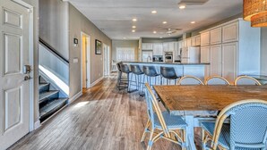 A spacious kitchen with a central island, bar stools, and a wooden dining table. - T's Treasure's - Eight-bedroom, eight-bath oceanfront duplex w/ pool (Surfside Beach)