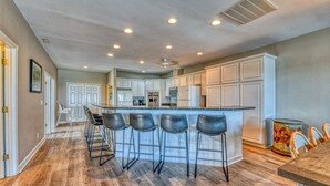 A modern kitchen with a central island, bar stools, and white cabinetry. - T's Treasure's - Eight-bedroom, eight-bath oceanfront duplex w/ pool (Surfside Beach)
