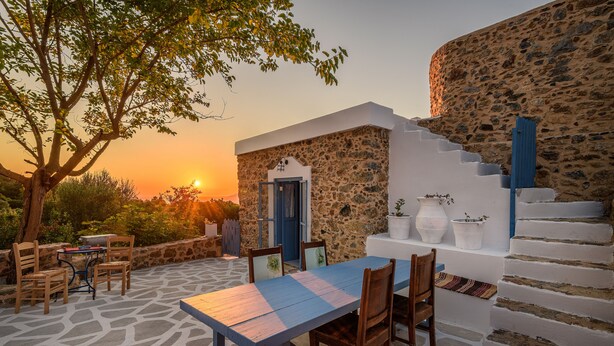A stone building with a staircase, a table with chairs, and a view of the sunset.