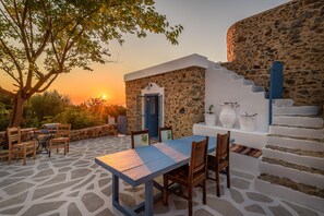 Un edificio de piedra con una escalera, una mesa con sillas y vistas al atardecer.