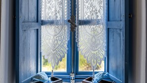 A window with blue shutters, lace curtains, and two small wooden drawers below.