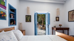 A bedroom with a bed, a nightstand, a dresser, and a blue shelf with books and pictures. There is a door leading to an outdoor area with a table and chairs.