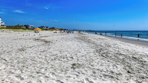 A wide sandy beach with umbrellas and people.