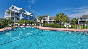 A swimming pool with clear blue water, surrounded by lounge chairs and a building with balconies.