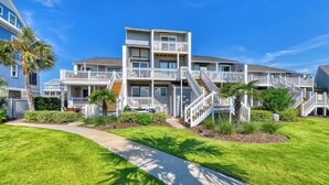 A multi-story residential building with a central staircase, balconies, and a well-maintained lawn.