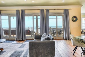 A living room with a sofa, a glass table, and a view of the ocean through large sliding glass doors.