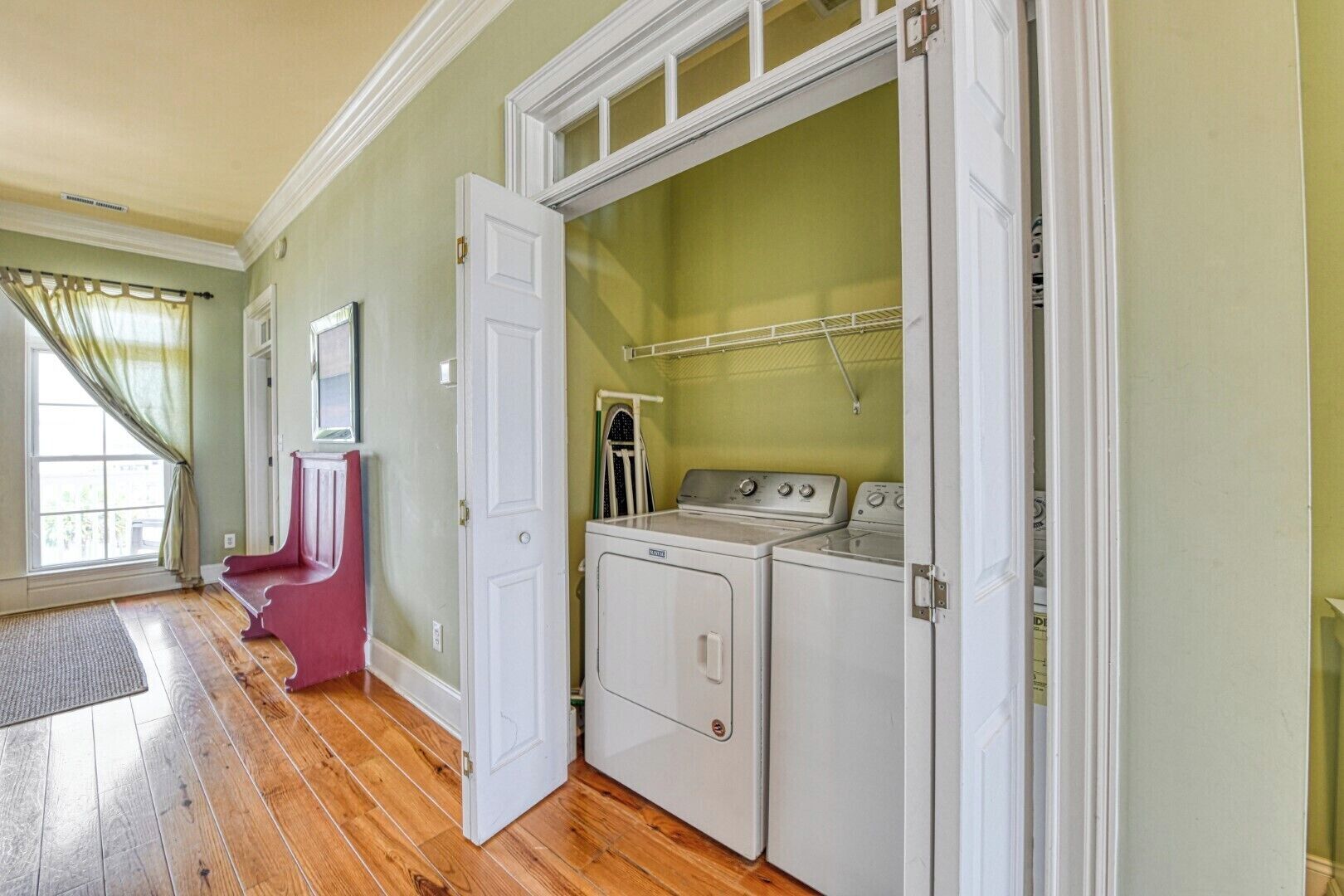 Un cuarto de lavado con lavadora y secadora, un banco rojo y una ventana con cortinas.
