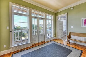 Quarto com piso de madeira, um banco e vista através de grandes janelas.