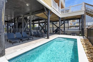 Un espace piscine avec des chaises longues, un barbecue et une terrasse couverte.