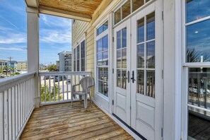 A covered porch with a wooden floor, a white chair, and a view of the street.