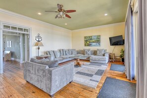 A spacious living room with a sectional sofa, a ceiling fan, a flat-screen TV, and a painting on the wall.