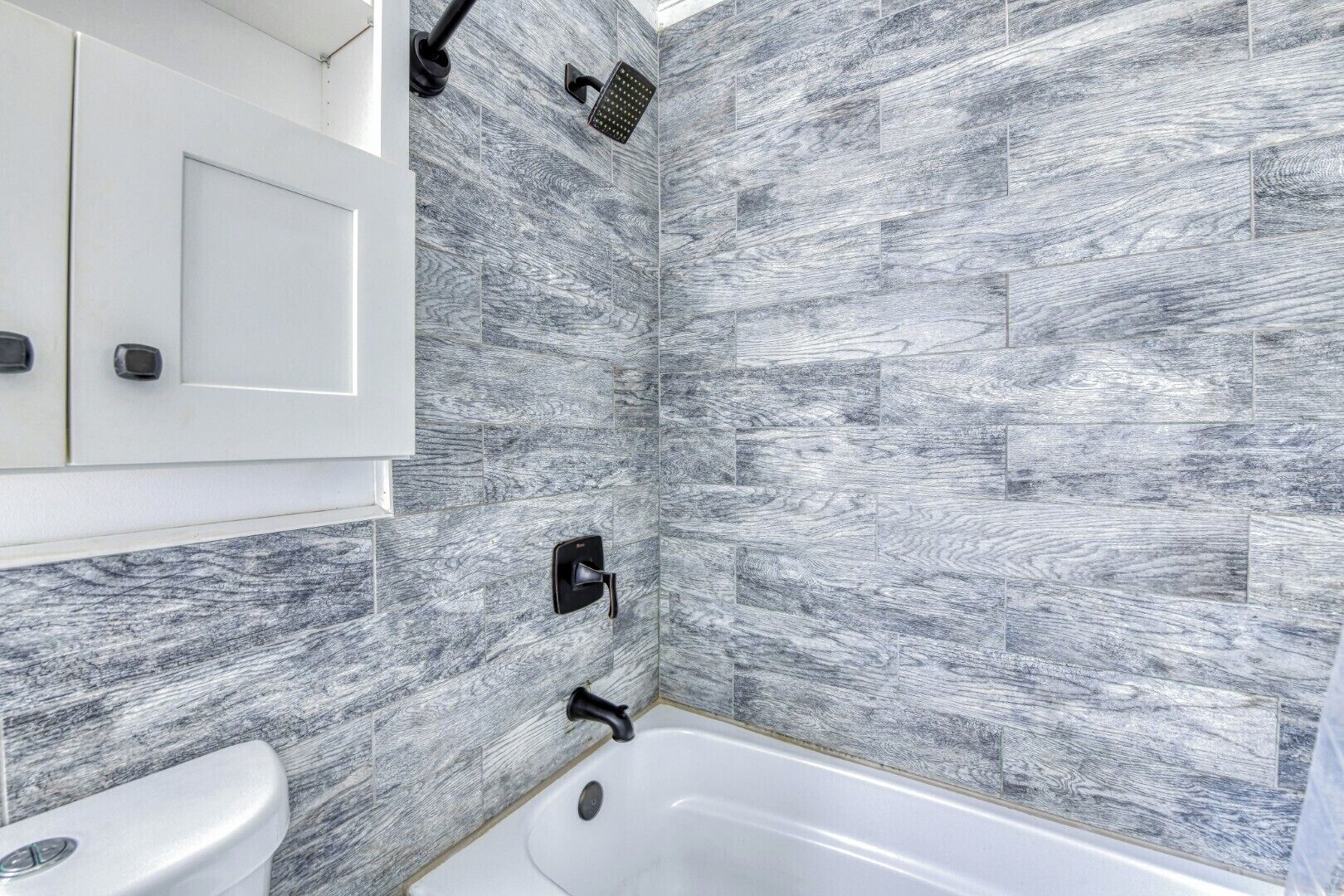 A bathroom with a white bathtub, a white toilet, and a shower with a black faucet.