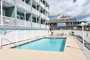 A pool area with a blue pool, white railings, and a building with balconies in the background. - Duneside III 304, Oceanfront Condo close to Garden City Pier (Garden City Beach)