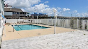 A pool area with a wooden deck, a white fence, and a pier in the background. - Duneside III 304, Oceanfront Condo close to Garden City Pier (Garden City Beach)
