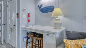 A compact room with a white desk, two stools, a lamp, a fire extinguisher, and a blue whale decoration on the wall. - Duneside III 304, Oceanfront Condo close to Garden City Pier (Garden City Beach)