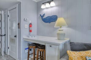 A compact room with a white desk, two stools, a lamp, a fire extinguisher, and a blue whale decoration on the wall. - Duneside III 304, Oceanfront Condo close to Garden City Pier (Garden City Beach)