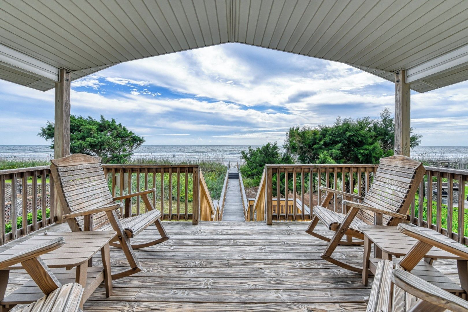 A wooden deck with a view of the ocean, featuring wooden chairs and tables.