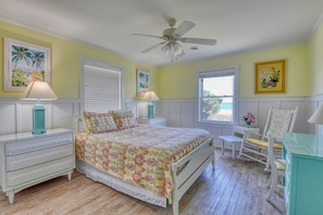 A bedroom with a bed, two bedside tables with lamps, a chair, a desk, and a ceiling fan.