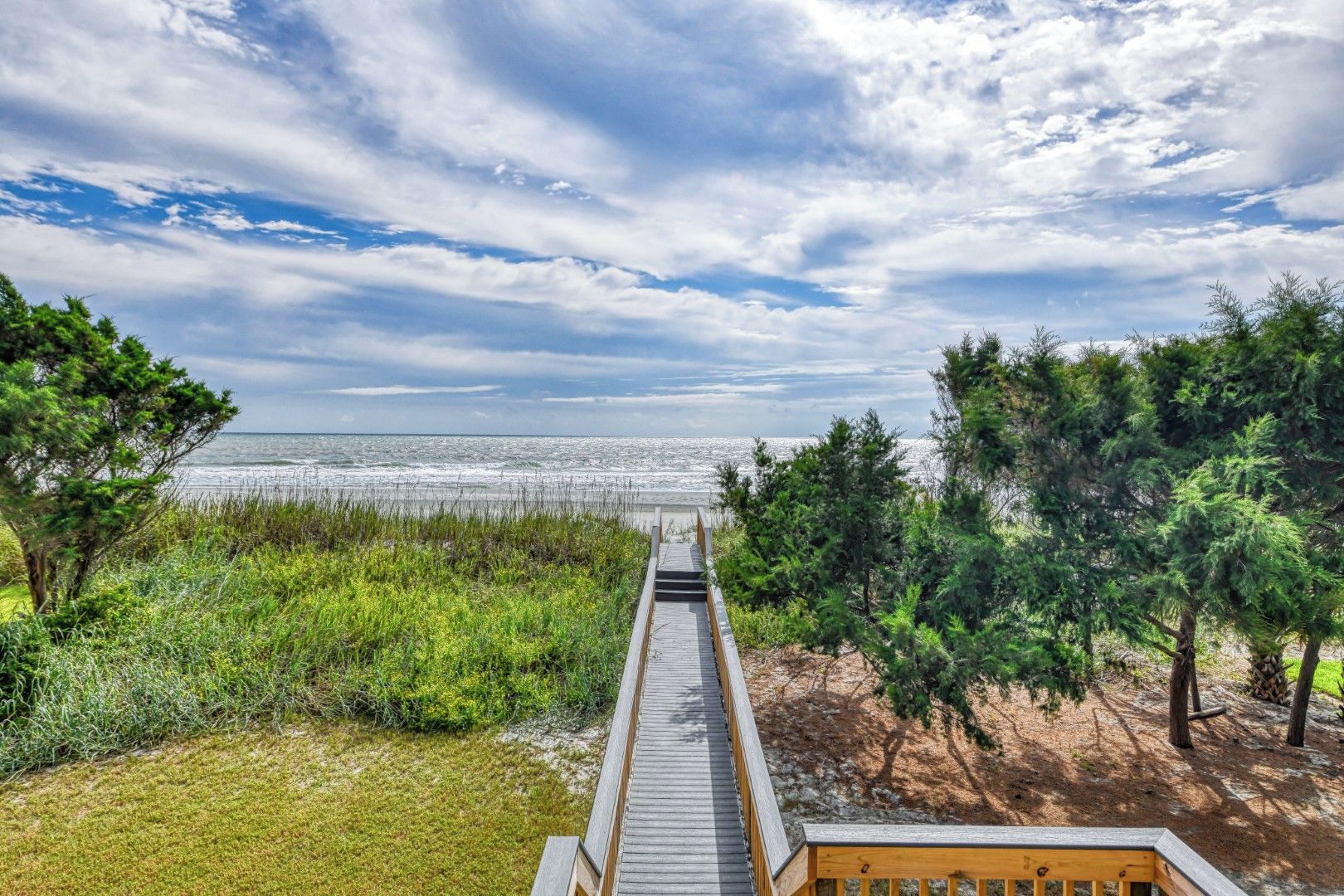 A wooden boardwalk leading to a beach with a view of the ocean and a cloudy sky.