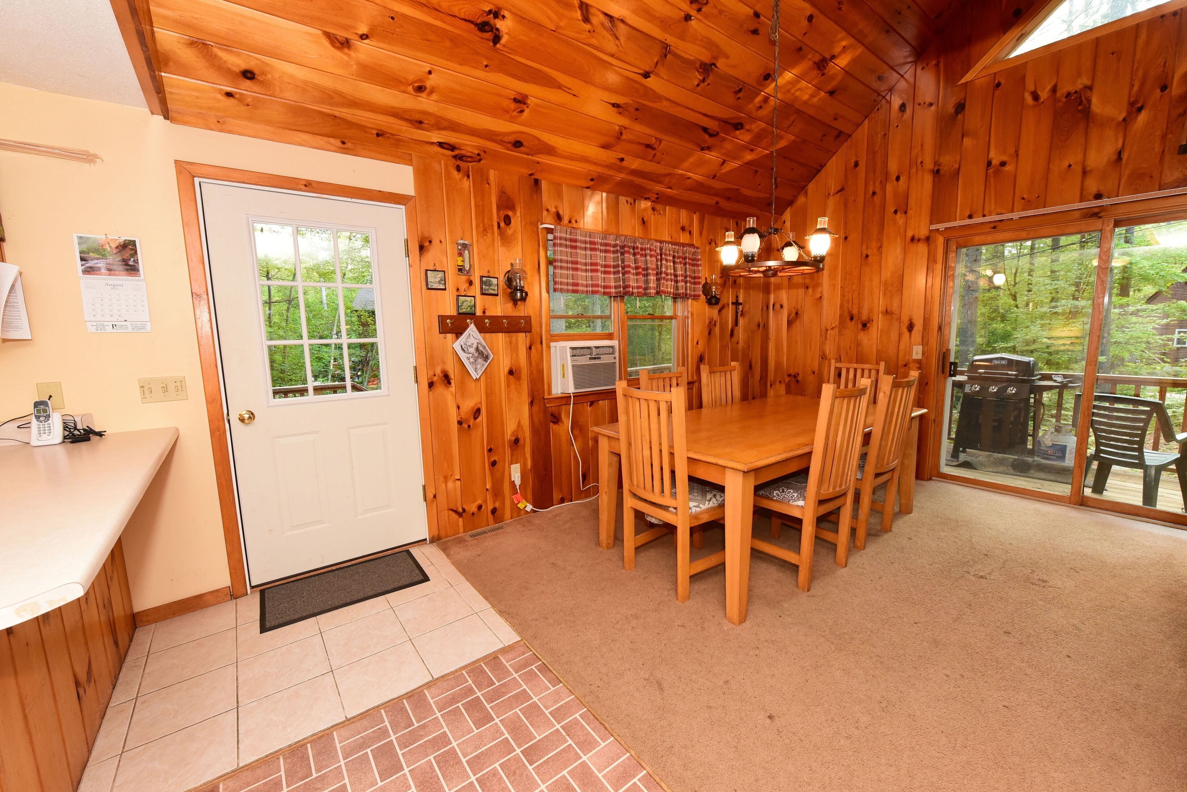A wooden interior with a dining area, a door, and a view through large windows.