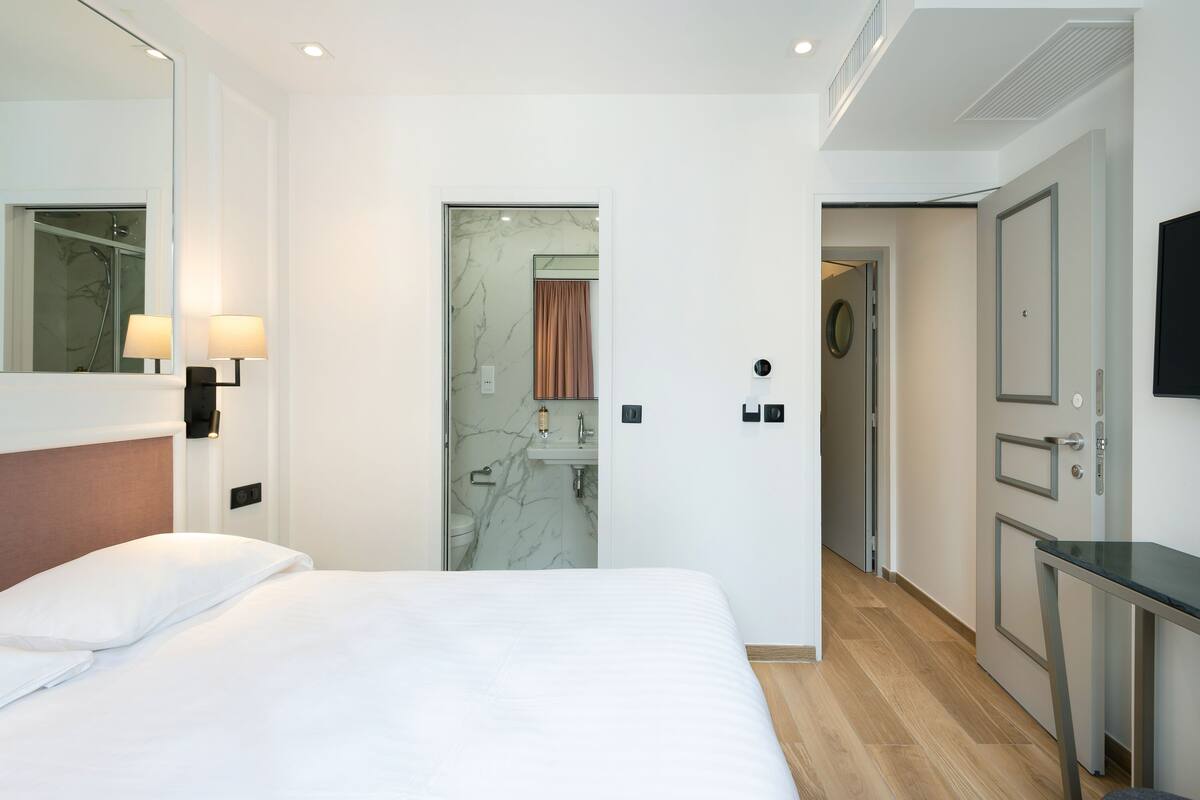 Habitación de hotel con una cama grande, un baño con pared de mármol y un televisor montado en la pared.