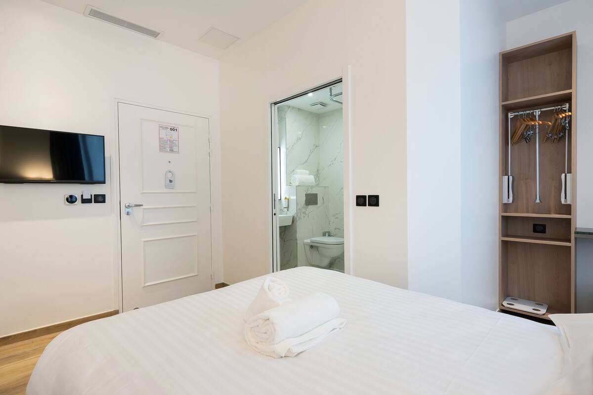 Habitación de hotel con cama, televisión, armario y baño visible a través de una puerta abierta.