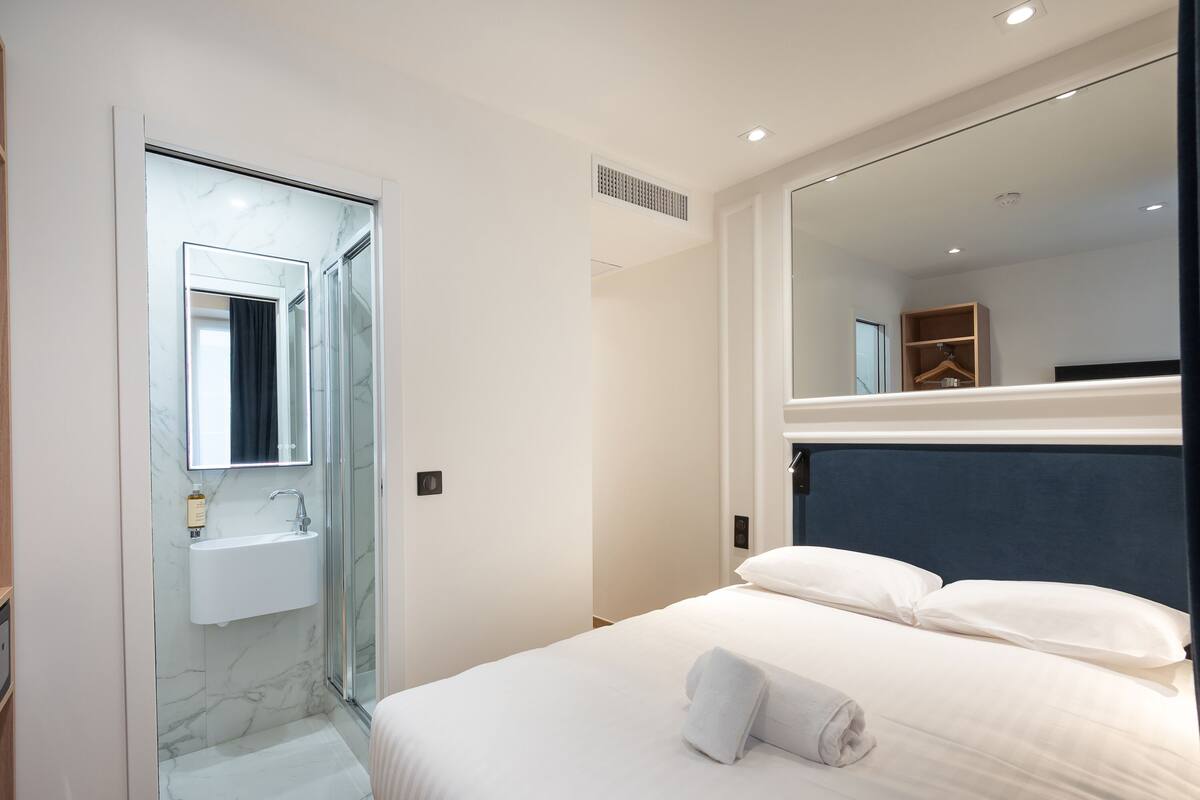 Una habitación de hotel moderna con una cama grande, un baño con lavamanos y un espejo.