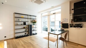 A modern kitchen with a wooden floor, a dining table with chairs, a black shelving unit with various items, and a large window with a view of the outside. - Hotel au coeur des Arts et Metiers (Paris)