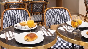 A modern kitchen with wooden cabinets, a refrigerator, and a dining area with wicker chairs and round tables. - Hotel au coeur des Arts et Metiers (Paris)