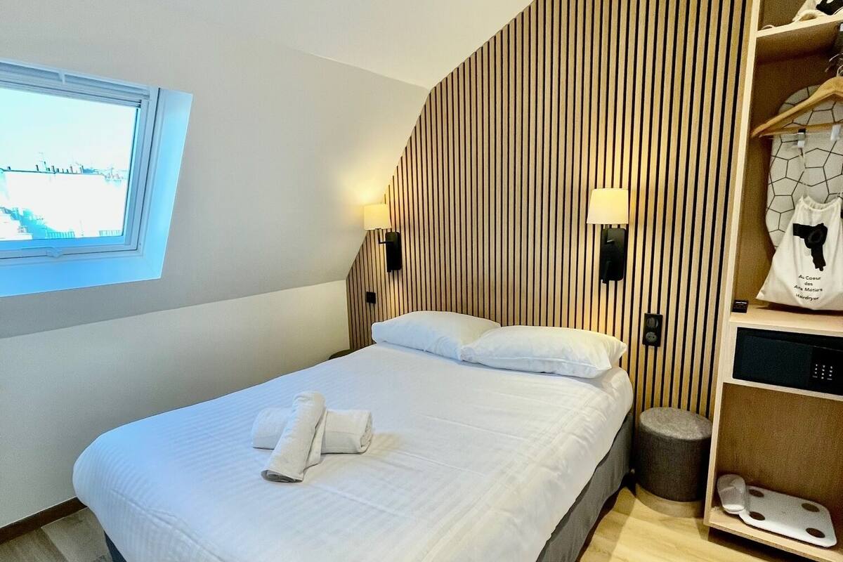 Un dormitorio moderno con una cama grande, una ventana, un panel de pared de listones de madera, una mesita de noche y un tocador.