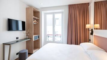 A modern hotel room with a bed, a TV, a desk, and a wardrobe.