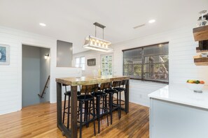A modern kitchen with a central island, bar stools, and a hanging light fixture. - Seas the Day: Stunning 6BR Isle of Palms Home with Private Pool! (Isle of Palms)