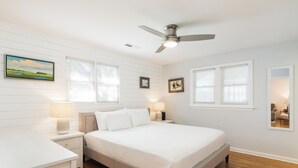Un dormitorio con cama, mesitas de noche, lámparas, ventilador de techo y ventana con persianas.