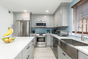 A modern kitchen with stainless steel appliances, a white countertop, and a window with blinds.