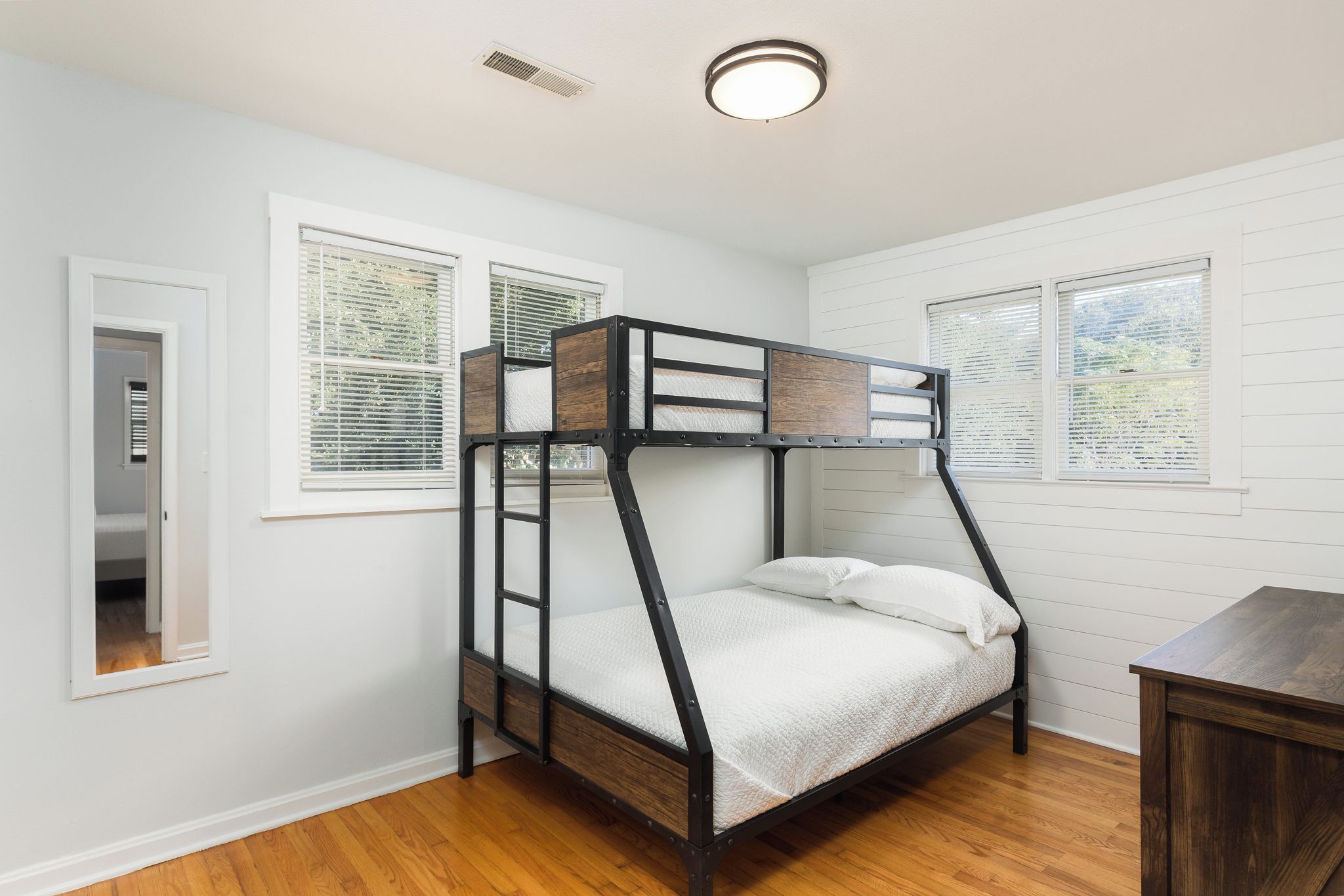 A bunk bed with a wooden frame and white bedding in a room with white walls and wooden flooring.