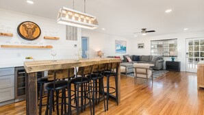 A modern kitchen with a wooden bar area, a dining table with bar stools, and a large decorative wall piece.
