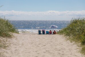 Un sentier de sable qui mène à des chaises de plage et à un parasol.