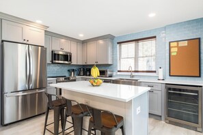 Una cocina moderna con electrodomésticos de acero inoxidable, una isla central con taburetes y una ventana con persianas.