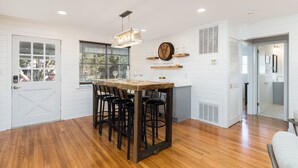 A modern kitchen with a wooden table, bar stools, and pendant lighting.