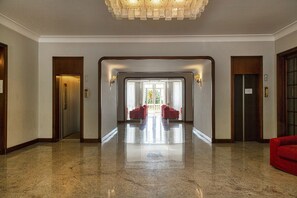 A spacious lobby with a polished marble floor, a central seating area with red chairs, and a view of the outdoors through a glass door.
